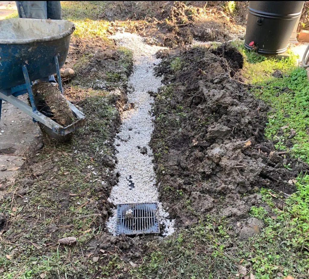 Gravel drainage run cut across the lawn with a catch basin grate set in to collect surface water
