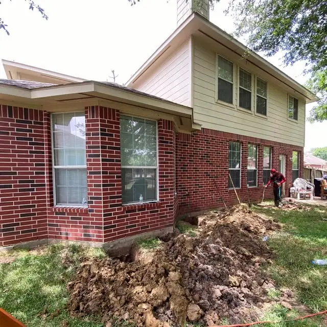 House leveling and foundation repair work in progress, with soil excavated along the exterior foundation. The exposed area provides access for stabilizing and leveling the home’s foundation.