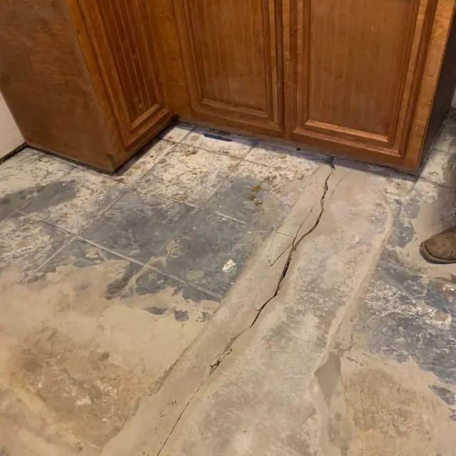 Foundation contractor working along an excavated section beside a residential home. The exposed area provides access for evaluating and repairing foundation settlement concerns.