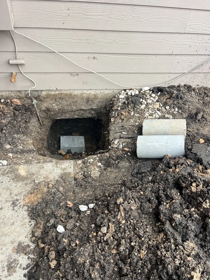 Excavated foundation access point with concrete pier sections ready for installation beneath a home. The repair helps stabilize areas affected by foundation settlement and shifting soil.