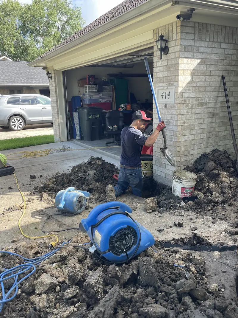 Foundation repair contractor working beside an excavated section of a residential home. Specialized equipment is being used during the foundation stabilization and repair process.