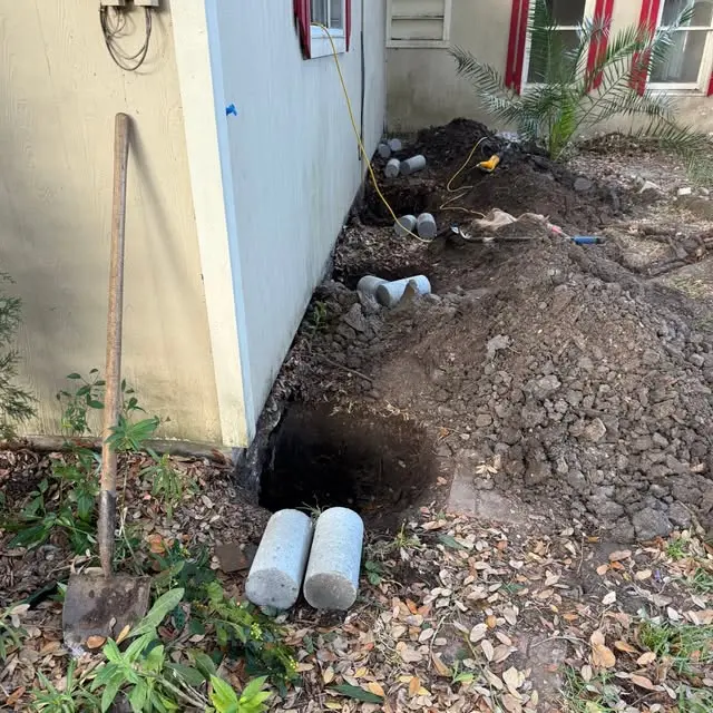 Foundation repair in progress with multiple excavated access points and concrete pier sections prepared beside a residential home. The work helps stabilize settled areas and restore proper foundation support.