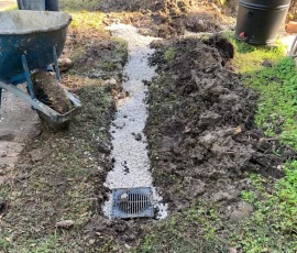 Gravel drainage run cut across the lawn with a catch basin grate set in to collect surface water