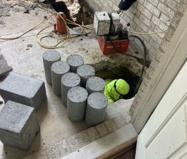 A stack of concrete piers at the door while one of our team works down in the hole