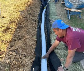 One of our crew bedding the pipe into a fabric-lined French drain trench