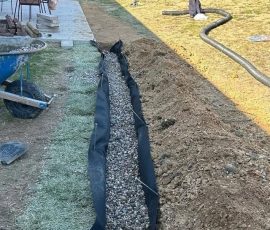 French drain trench packed with gravel and wrapped in filter fabric before backfill