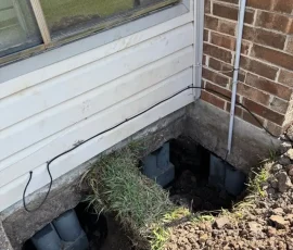 Foundation repair in progress with excavated access points and concrete piers installed beneath the home. The exposed area provides access for stabilizing settled sections of the foundation.