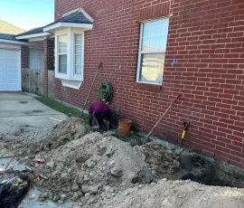 Professional foundation repair contractor working along an excavated section of a residential slab. Proper foundation repairs require experienced crews and specialized methods to stabilize the home safely.